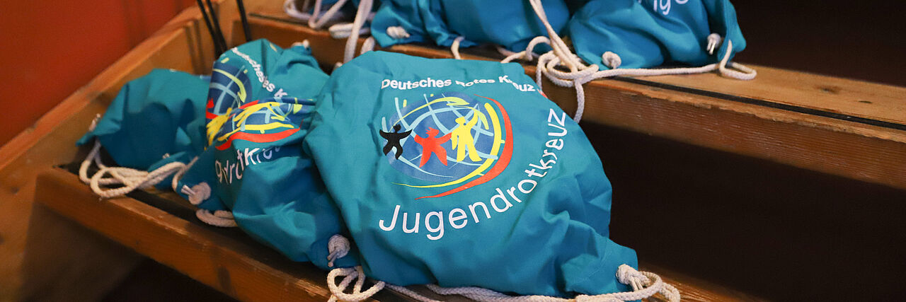 Mehrere Rucksäcke im JRK-Design liegen auf einer hölzernen Treppe.